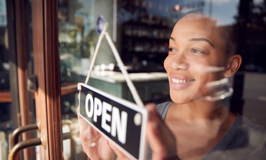 Female owner in window of start up coffee shop or restaurant turning round open sign on door.