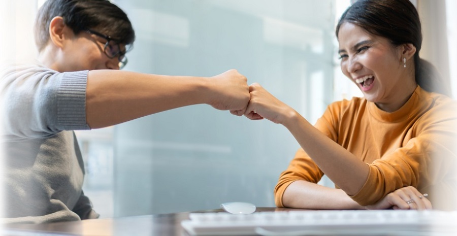 Businessman and businesswoman fist bumping while working in an office together.