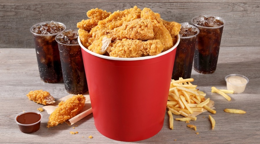 Fried chicken in a red bucket with sides and drinks surrounding it.