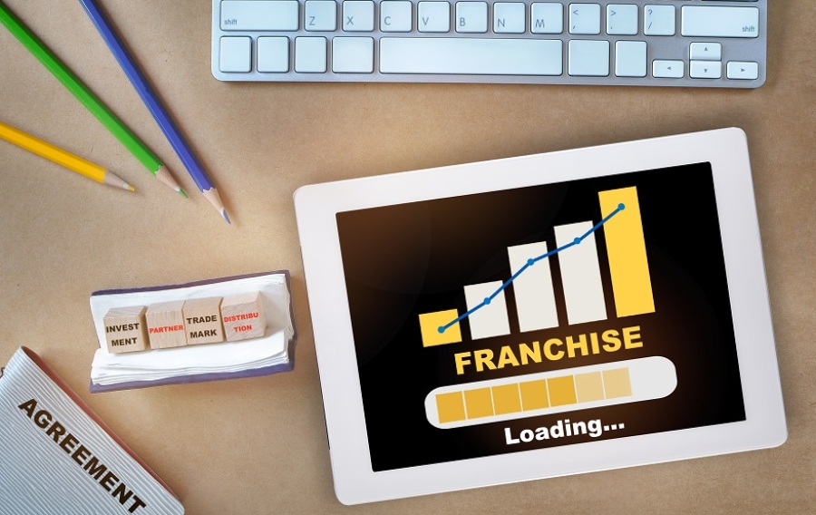 Franchise business growth graph on digital tablet with keyboard, pencils, and agreement. Four blocks present say: Investment, Partner, Trademark and Distribution.