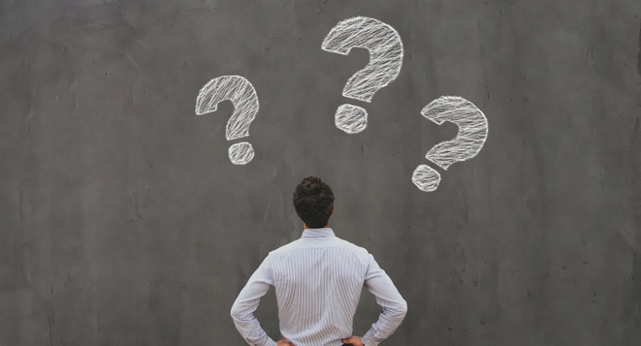 Man looking up at a grey background with three question marks.