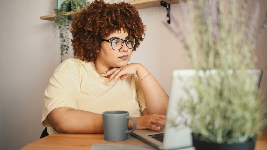 Black woman with curly afro hair and glasses working on laptop computer at home.