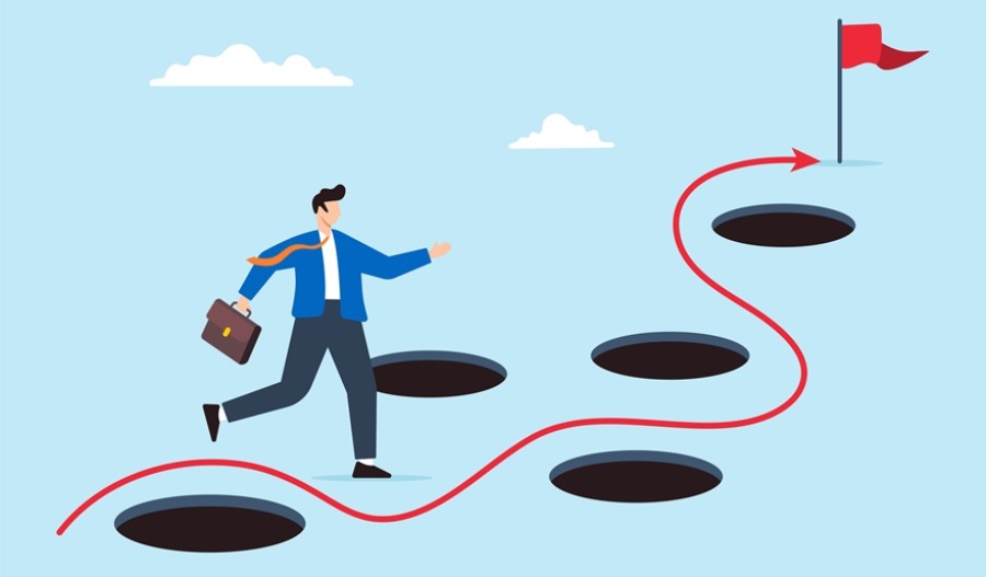 Businessman avoiding numerous pitfalls en route to the goal of a red flag representing business success.