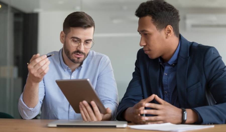 Two businessmen sitting a table having a discussion. The guy on the left is holding a tablet and explaining something to the guy on the right.