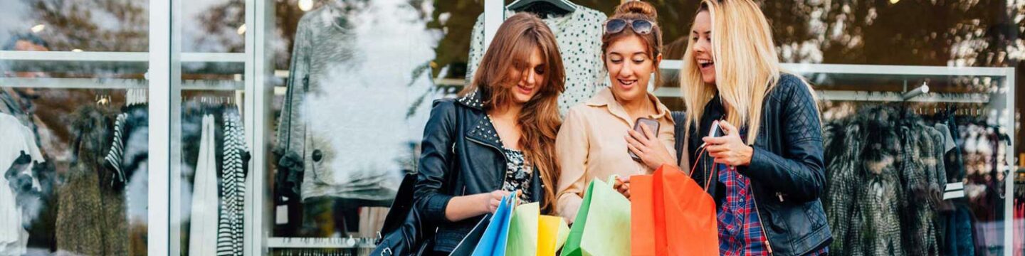 Women with shopping bags smiling at a retail clothing store