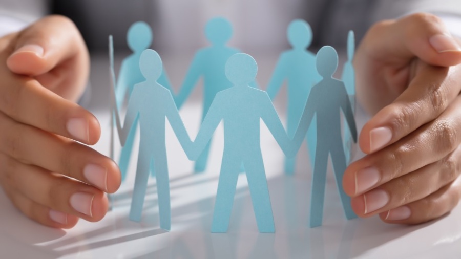 Close-up of a businessperson's hand protecting a group of paper cutout figures.