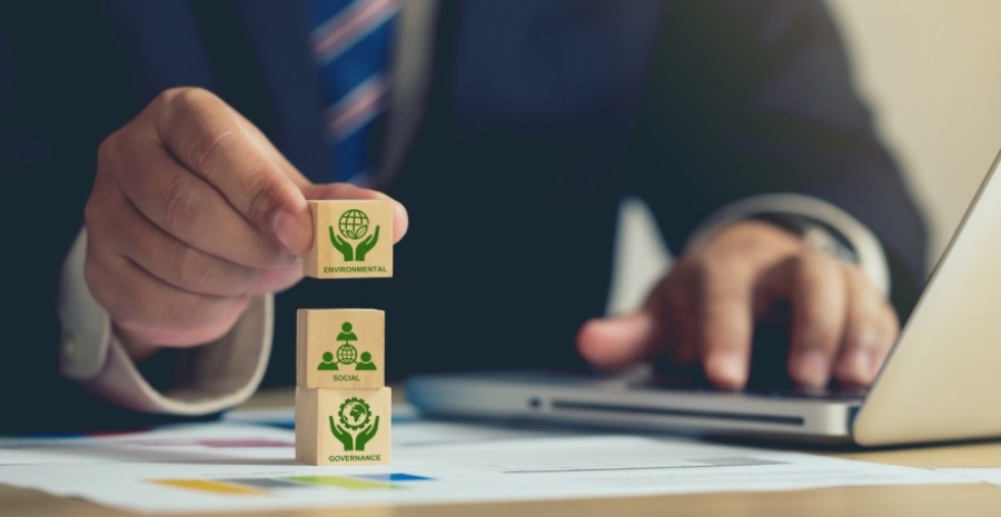 Businessman stacking wooden cube blocks with ESG (environmental, social, governance) icons on them.