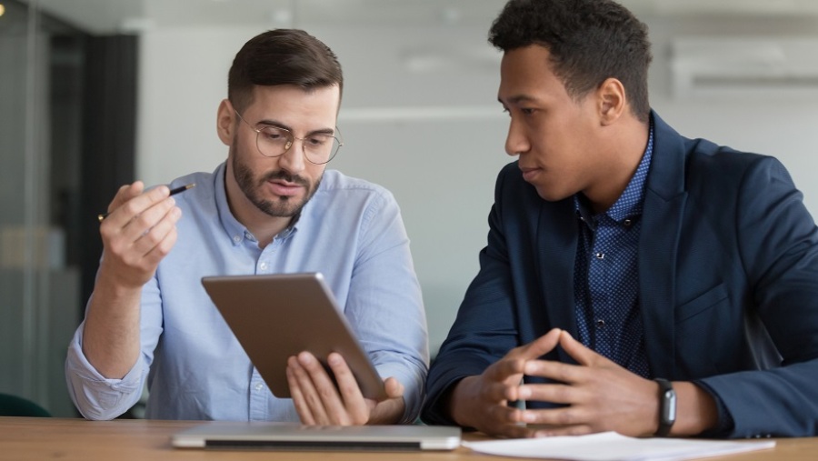 Two businessmen having a discussion. One is holding a tablet and explaining something while the other looks on and is listening.