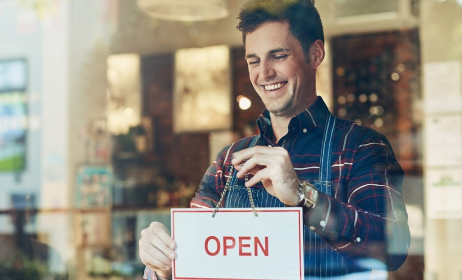 Shot of a smiling young male business owner hanging up an open sign in a shop window.