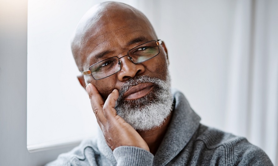 Older Black man looking thoughtful while his head rests in his right hand.
