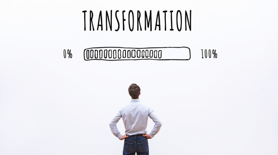 Young business man looking up at a progress bar with the word "Transformation" above it. The bar is approximately 75% complete.
