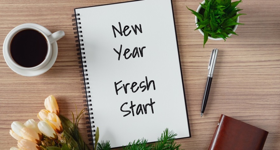 Notebook with the words "New Year, Fresh Start" on table. There is also a cup of coffee on the table with flowers and a pen.