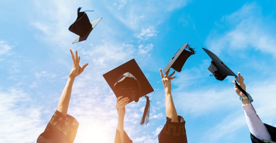 Four graduates throwing graduation hats in the air.