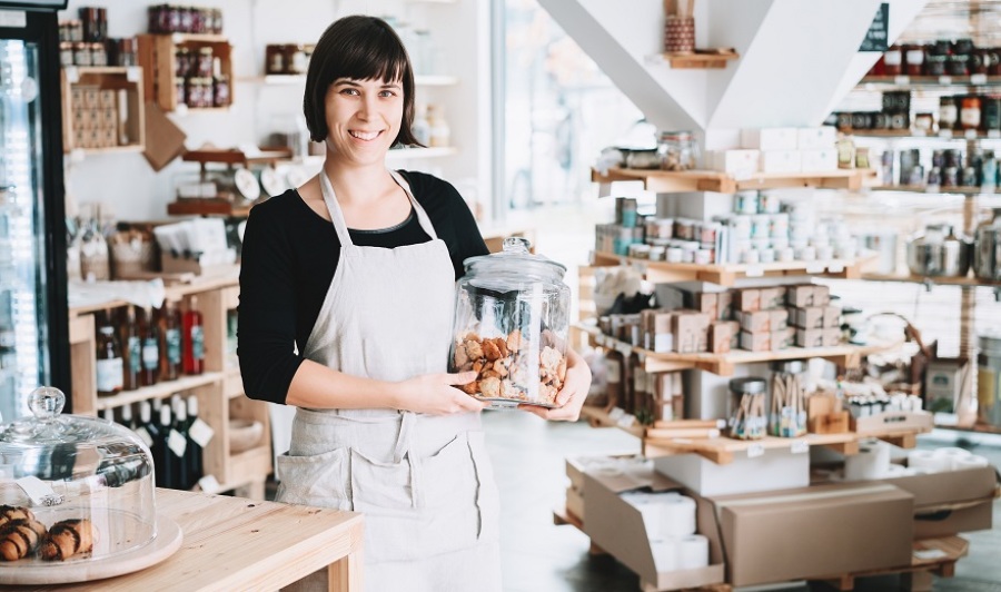 Smiling female small local business owner standing in front of counter holding jar of baked goods.