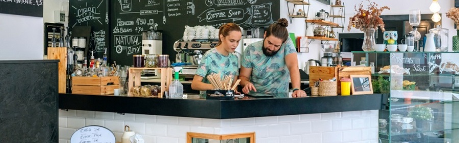 Owners of a coffee shop working together looking at a tablet while leaning on the counter.