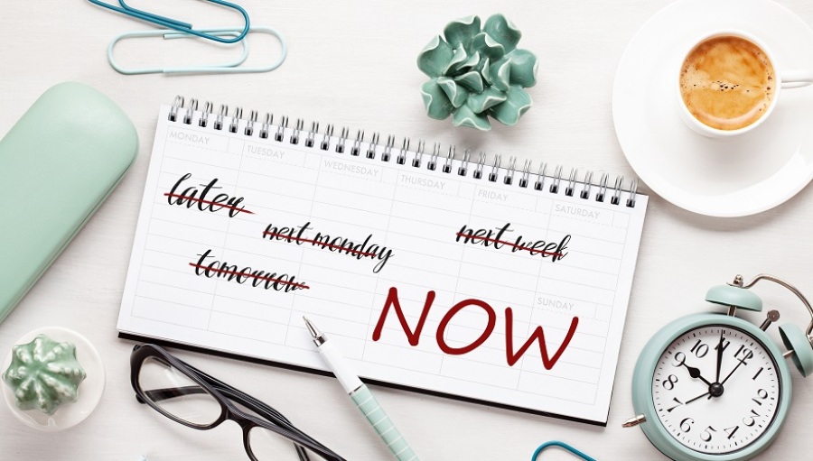 Concept of time management with notes in a weekly organizer on top of a desk with coffee, glasses, alarm clock and other related items surrounding it.