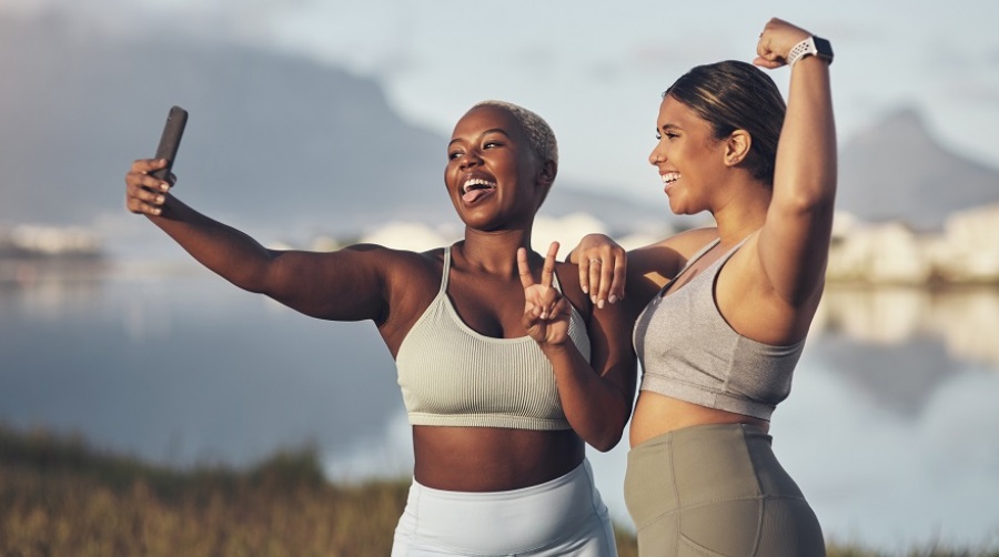 Two women smiling and flexing while talking a selfie during a workout.