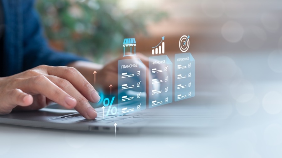 Person typing on a laptop with holographic franchise documents, growth chart, and target icon. Concept of franchise investment analysis and business opportunity review.