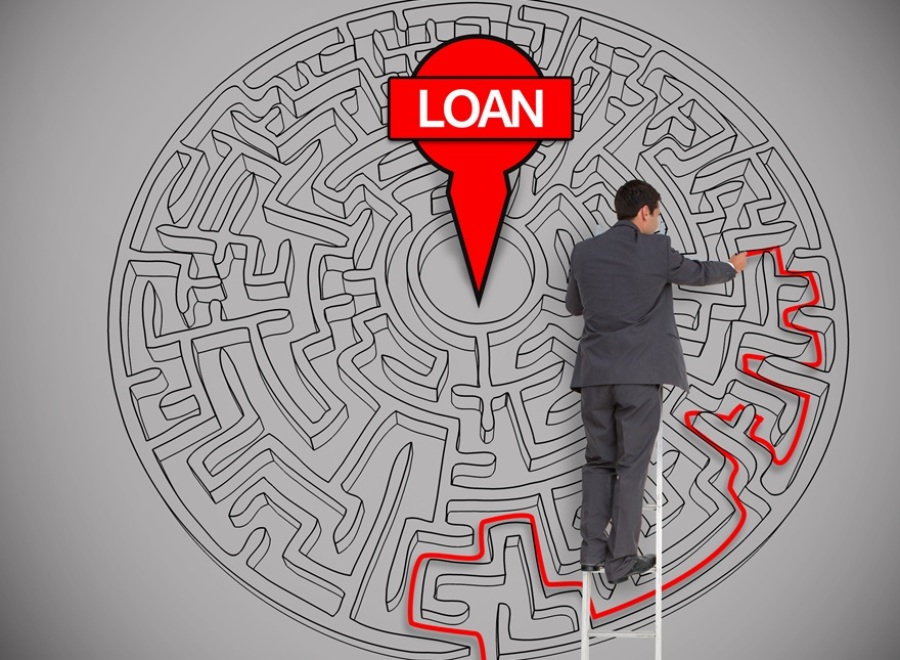 Businessman on ladder trying to find a loan in a maze on grey wall.