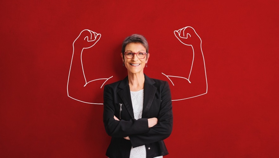 Adult woman standing in front of a red wall with flexed arms drawn behind her.